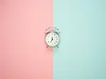 Waiting after your egg retrieval for fertilization & embryo development results can be stressful. Image of clock lying on a surface which is half baby blue and half baby pink.